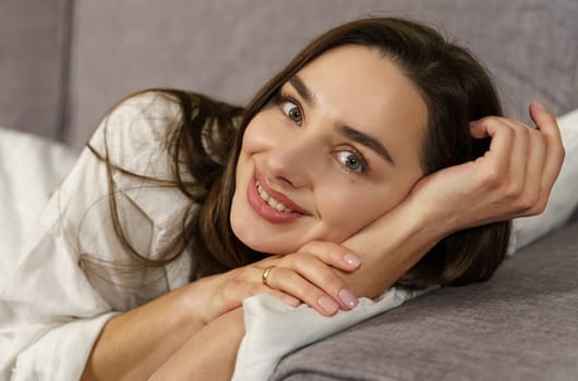 Young beautiful woman lies on the sofa, looks at the camera, smiles.