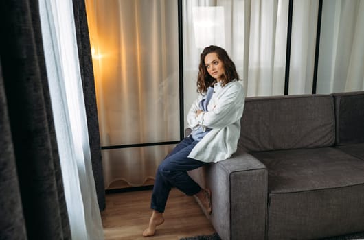 Portrait of a beautiful young woman who sits on the back of the sofa and smiles.