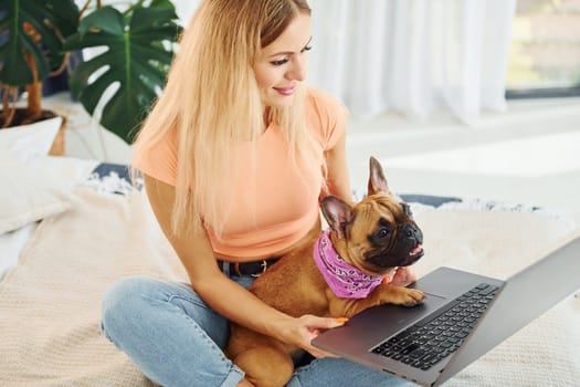 Using laptop. Woman with pug dog is at home at daytime.