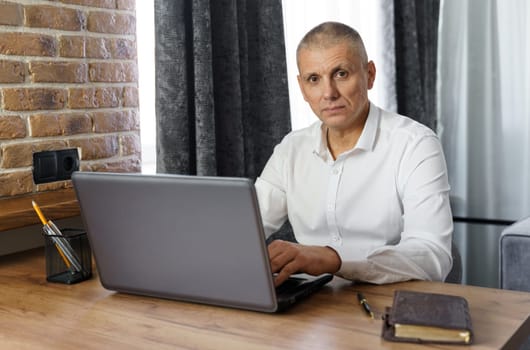 Portrait of middle aged business man working at home with laptop. Remote business concept.