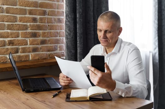 A businessman holds a phone in his hands, reads a bank receipt, documents. Financial manager, company.