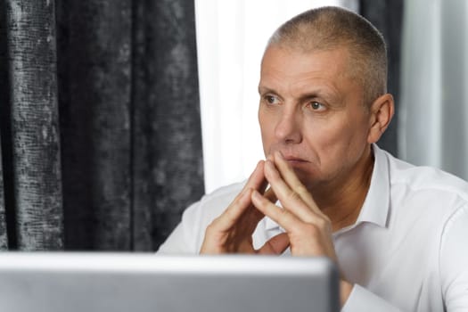 Pensive businessman, manager creates new business ideas while sitting at a table with a laptop. Close-up.