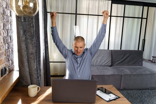 A businessman working at a computer rejoices in a perfect successful transaction, raising his hands up. The concept of success.