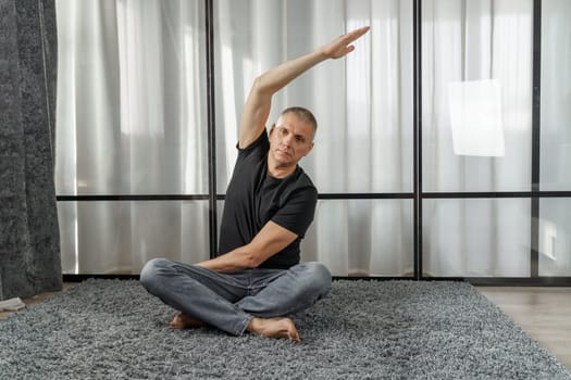 A man sits on a mat and does yoga, does exercises. Healthy lifestyle.