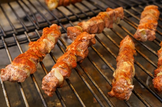 Fried meat with onions on a skewer lies on the grate. Polish street food.