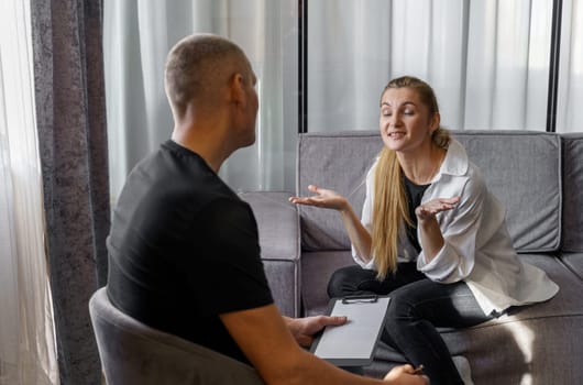 A man psychologist carefully listens to the patient - a woman who emotionally talks about himself, makes notes.