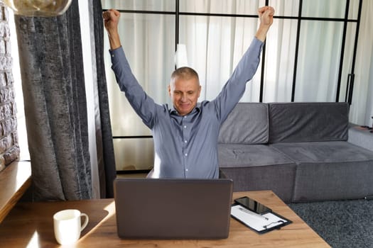 A businessman working at a computer rejoices in a perfect successful transaction, raising his hands up. The concept of success.