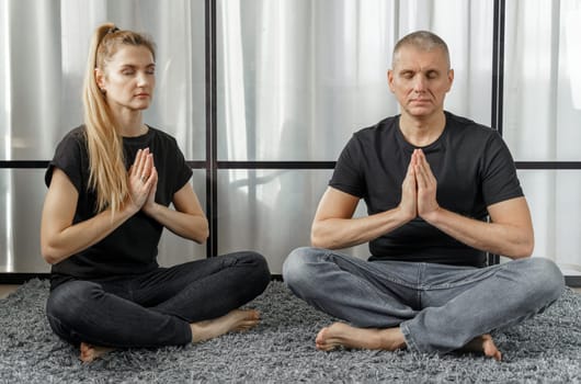 Man and woman practice yoga and meditate for relaxation and balance of life on a mat in a room at home. Sports concept.