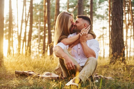 Sitting on the ground. Happy couple is outdoors in the forest at daytime.