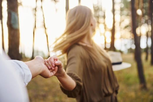 Woman holding man's hand. Happy couple is outdoors in the forest at daytime.