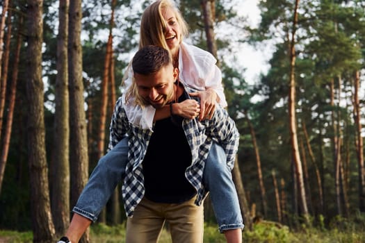 Woman is riding her man. Happy couple is outdoors in the forest at daytime.
