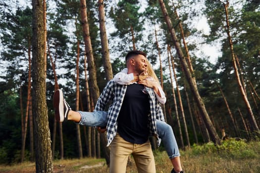 Woman is riding her man. Happy couple is outdoors in the forest at daytime.