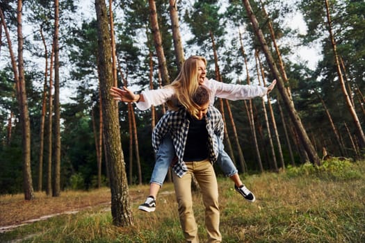 Woman is riding her man. Happy couple is outdoors in the forest at daytime.