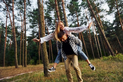 Woman is riding her man. Happy couple is outdoors in the forest at daytime.