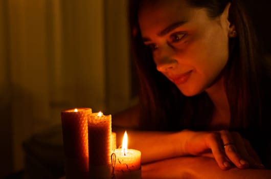 A woman holds a burning candle in her palms on a dark black background.