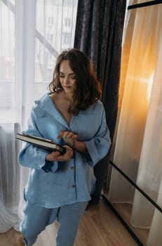 A young woman in a dark blue suit stands in a room with a tablet in her hands. Browses online stores, social networks. Vertical frame.