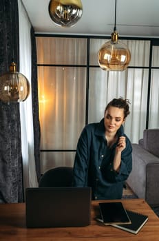 Portrait of a business woman standing near the desk. Notepad, tablet and laptop on the table. Vertical frame.