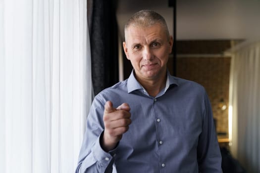 Confident smiling businessman in a blue shirt pointing his index finger at the camera. The concept of people and gestures.