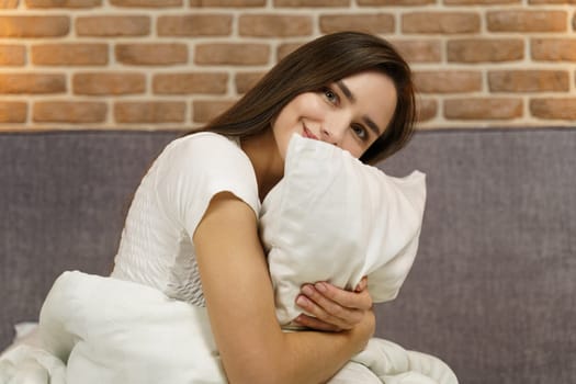 Young woman hugging a pillow on a comfortable bed with white linens.