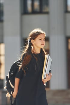 Against building. Schoolgirl is standing outside.