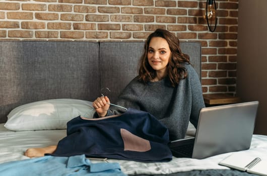 A young woman sits on a bed and admires her purchases made through an online store.