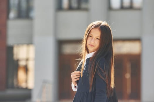 Against building. Schoolgirl is standing outside.