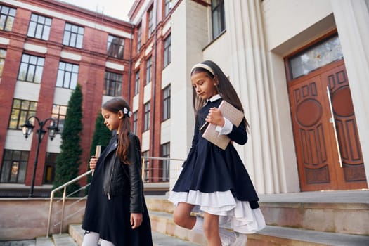 Conception of education. Two schoolgirls is outside together near school building.