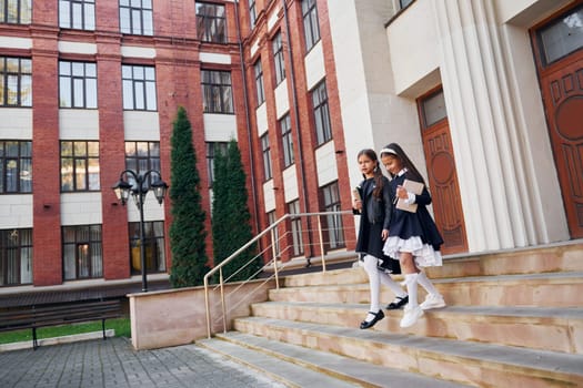 Conception of education. Two schoolgirls is outside together near school building.
