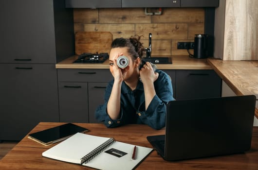 Portrait of a beautiful cheerful female clothing stylist who sits at a table near a laptop and looks through large spools of thread.