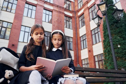 With books. Two schoolgirls is outside together near school building.
