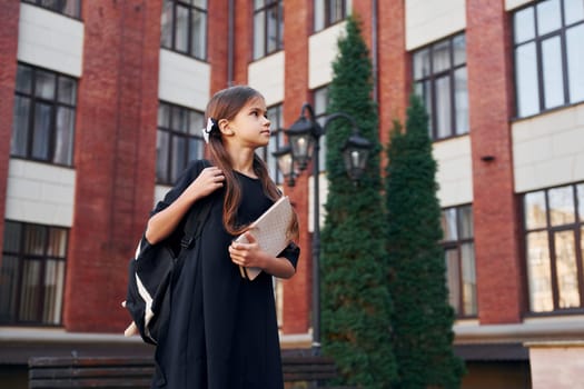 In formal uniform. Schoolgirl is outside near school building.