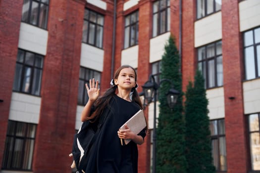 In formal uniform. Schoolgirl is outside near school building.