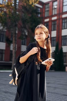 After lessons. Schoolgirl is outside near school building.