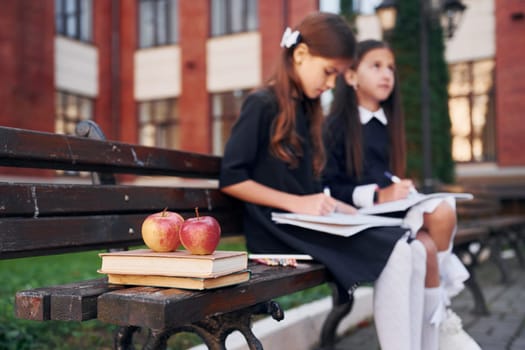 Books and apples. Two schoolgirls is outside together near school building.