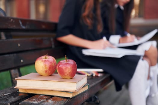 Apples is on the book. Two schoolgirls is outside together near school building.