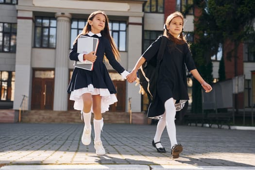 Two schoolgirls is running outside together near school building.