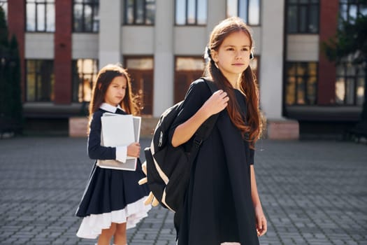 Front view. Two schoolgirls is outside together near school building.