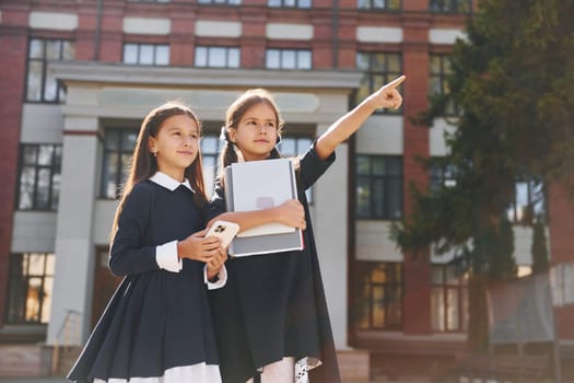 Two schoolgirls is outside together near school building.