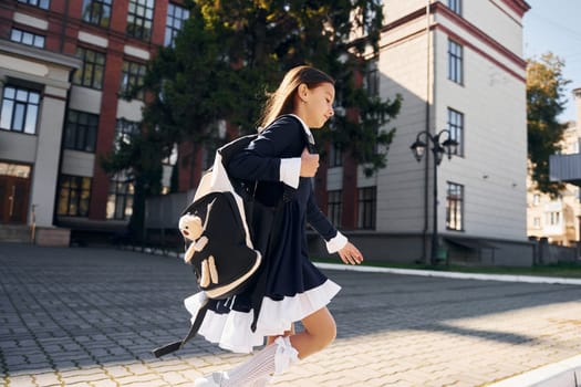 Having a walk. Schoolgirl is outside near school building.