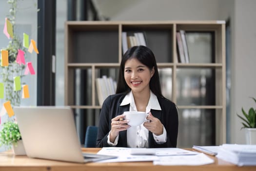 Happy young business Asian girl working at a office with coffee and laptop.