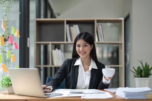 Happy young business Asian girl working at a office with coffee and laptop.