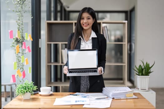 attractive Asian young business woman at her office desk workspace with a notebook laptop computer. Notebook blank screen mockup.