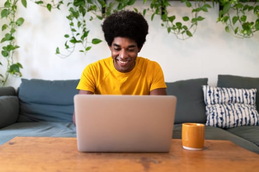 Smiling young african american man sitting on the sofa checking email with laptop. Technology concept. At home concept.