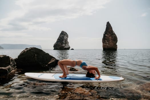 Woman sup yoga. Middle age sporty woman practising yoga pilates on paddle sup surfboard. Female stretching doing workout on sea water. Modern individual hipster outdoor summer sport activity