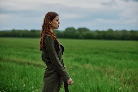 a beautiful, red-haired girl in a raincoat stands in a field in the spring in rainy weather. High quality photo