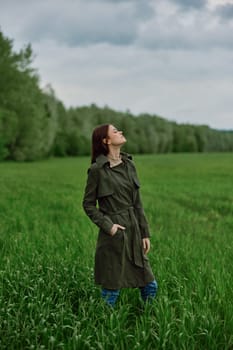 a beautiful woman in a dark coat stands in a green field in the spring in rainy weather. High quality photo