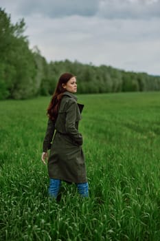 a beautiful woman in a dark coat stands in a green field in the spring in rainy weather. High quality photo