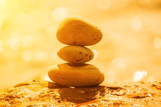 Balanced Pebbles Pyramid on the Beach on Sunny Day and Clear Sky at Sunset. Blue Sea on Background Selective focus, zen stones on sea beach, meditation, spa, harmony, calm, balance concept.