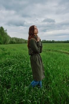 a beautiful woman in a dark coat stands in a green field in the spring in rainy weather. High quality photo