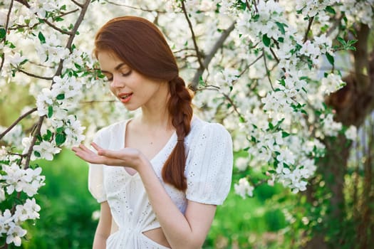 a beautiful woman in a light dress enjoys the spring while standing next to a flowering tree. High quality photo